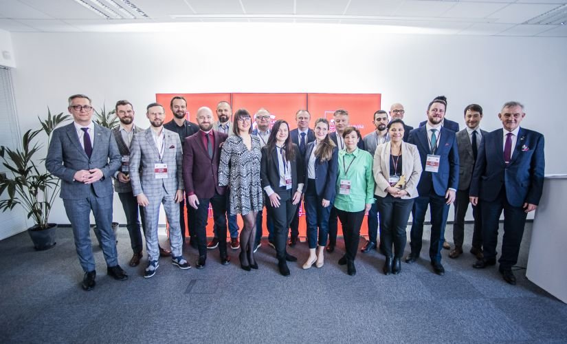 grupa kobiet i mężczyzn w średnim wieku stojąca  na tle ścianki z logo jubileuszu Politechniki łódzkiej